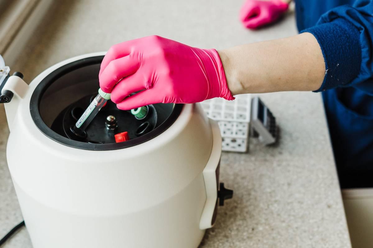 Gloved hand placing a blood draw vial into a centrifuge